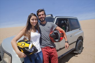 Hispanic couple holding helmets leaning on sports utility vehicle