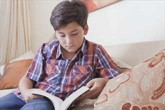 Hispanic boy reading book on sofa