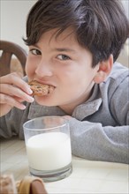 Hispanic boy eating cookie with milk at table