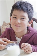 Hispanic boy eating cookie with milk at table