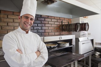 Smiling Hispanic chef posing near cheesecakes in oven