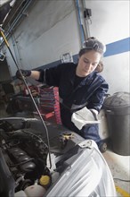 Hispanic mechanic checking oil in car engine