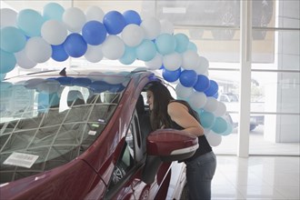 Hispanic woman examining car in dealership showroom