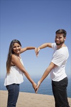 Hispanic couple making heart-shape with arms at beach