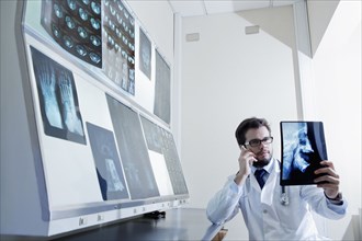 Hispanic doctor talking on cell phone examining x-ray
