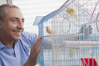 Smiling Hispanic man admiring birds in birdcage