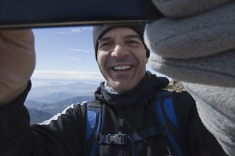Hispanic man posing for cell phone selfie on mountain