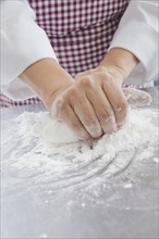Hands of Hispanic woman kneading dough in flour