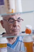 Hispanic man examining pill bottle from medicine cabinet