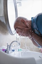 Hispanic man splashing water on face in bathroom