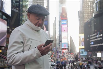 Hispanic man texting on cell phone in crowded city