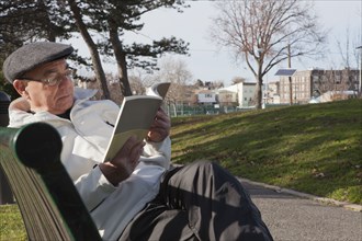 Hispanic man sitting on park bench reading book