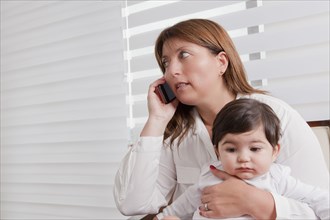 Hispanic mother holding baby boy and talking on cell phone