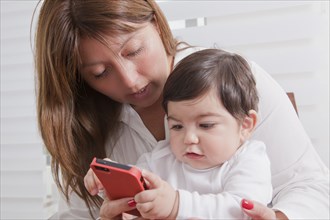 Hispanic mother holding baby boy playing with cell phone