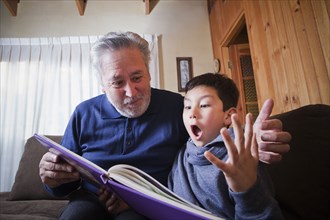 Hispanic grandfather and excited grandson reading book