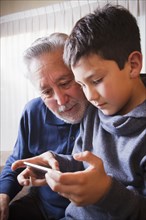Hispanic grandfather and grandson texting on cell phone