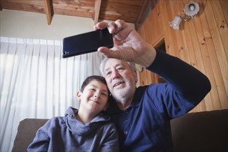 Hispanic grandfather and grandson posing for cell phone selfie