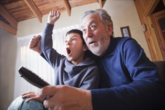 Hispanic grandfather and grandson cheering for soccer game on television