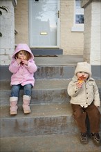 Caucasian brother and sister eating cupcakes on front stoop