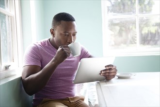 Black man drinking coffee and using digital tablet