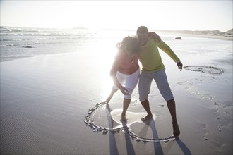 Couple drawing heart in sand on beach