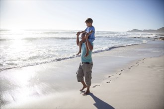 Mixed race father carrying son on shoulders on beach