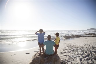 Mixed race father and children sitting on beach