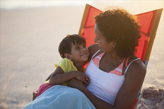 Mixed race mother and daughter hugging in chair on beach