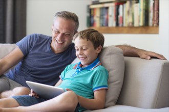 Caucasian father and son using digital tablet on sofa