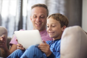 Caucasian father and son using digital tablet on sofa