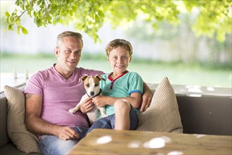 Caucasian father and son sitting with dog on sofa