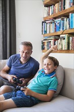 Caucasian father and son playing video games on sofa