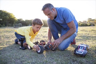 Caucasian father and son playing with remote control cars in field
