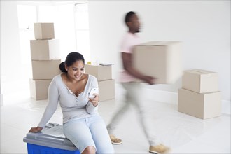 Woman relaxing with man carrying boxes in new home