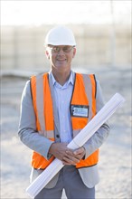 Caucasian architect holding blueprints at construction site