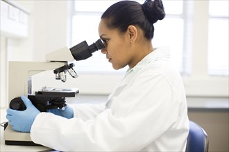 Mixed race scientist using microscope in laboratory