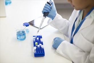 Mixed race scientist pipetting sample into tube in laboratory