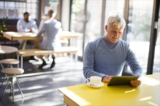 Older man using digital tablet in cafe