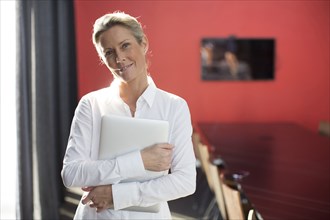 Caucasian businesswoman carrying laptop in conference room