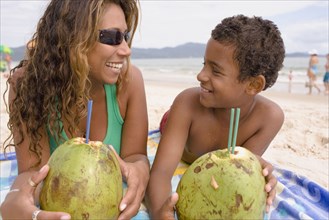 Hispanic mother and son lying on the beach drinking from coconuts