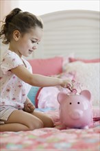 Young girl putting money in piggy bank