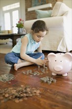 Young girl counting money next to piggy bank
