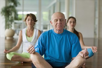 Senior man and two women meditating at health club