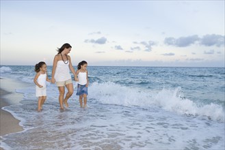 Multi-ethnic mother and daughters walking through ocean surf