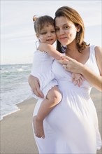 Pregnant mother holding daughter at beach