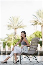 Hispanic woman sitting in chair on pier
