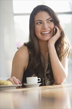 Hispanic woman drinking coffee and talking on cell phone