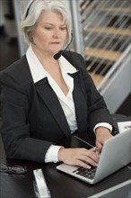 Smiling Businesswoman in headset typing on laptop