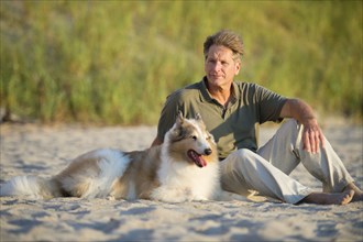 Caucasian man sitting with dog on beach