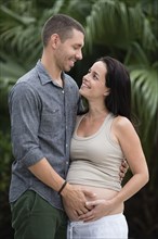 Man holding pregnant wife's belly outdoors